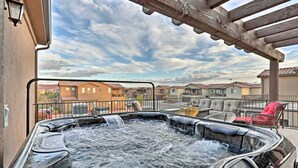 Un jacuzzi con una pérgola de madera encima, rodeado de mobiliario exterior y vistas a edificios vecinos.