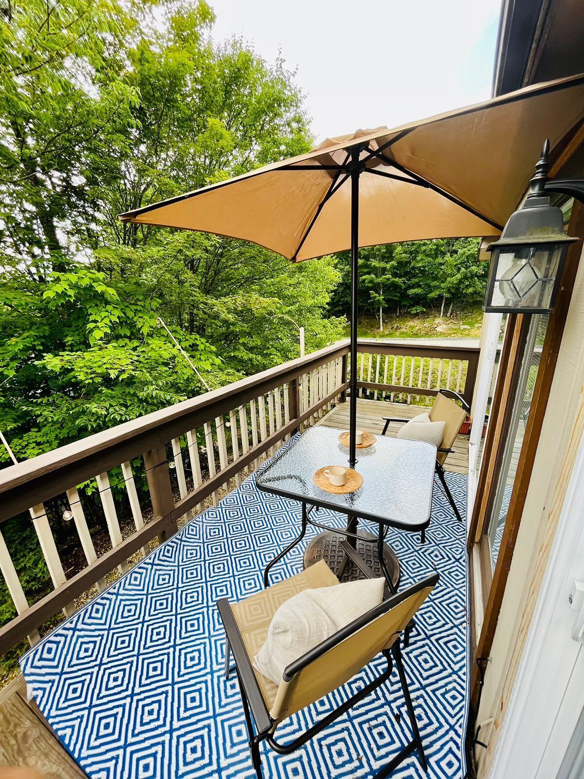 A balcony with a patterned floor, a table with chairs, and a large umbrella.