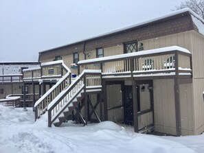 A building with a covered outdoor area, a staircase leading to a deck, and a snow-covered ground. - Cozy Pet-Friendly Studio! Land of Oz ! Festivals! (Beech Mountain)