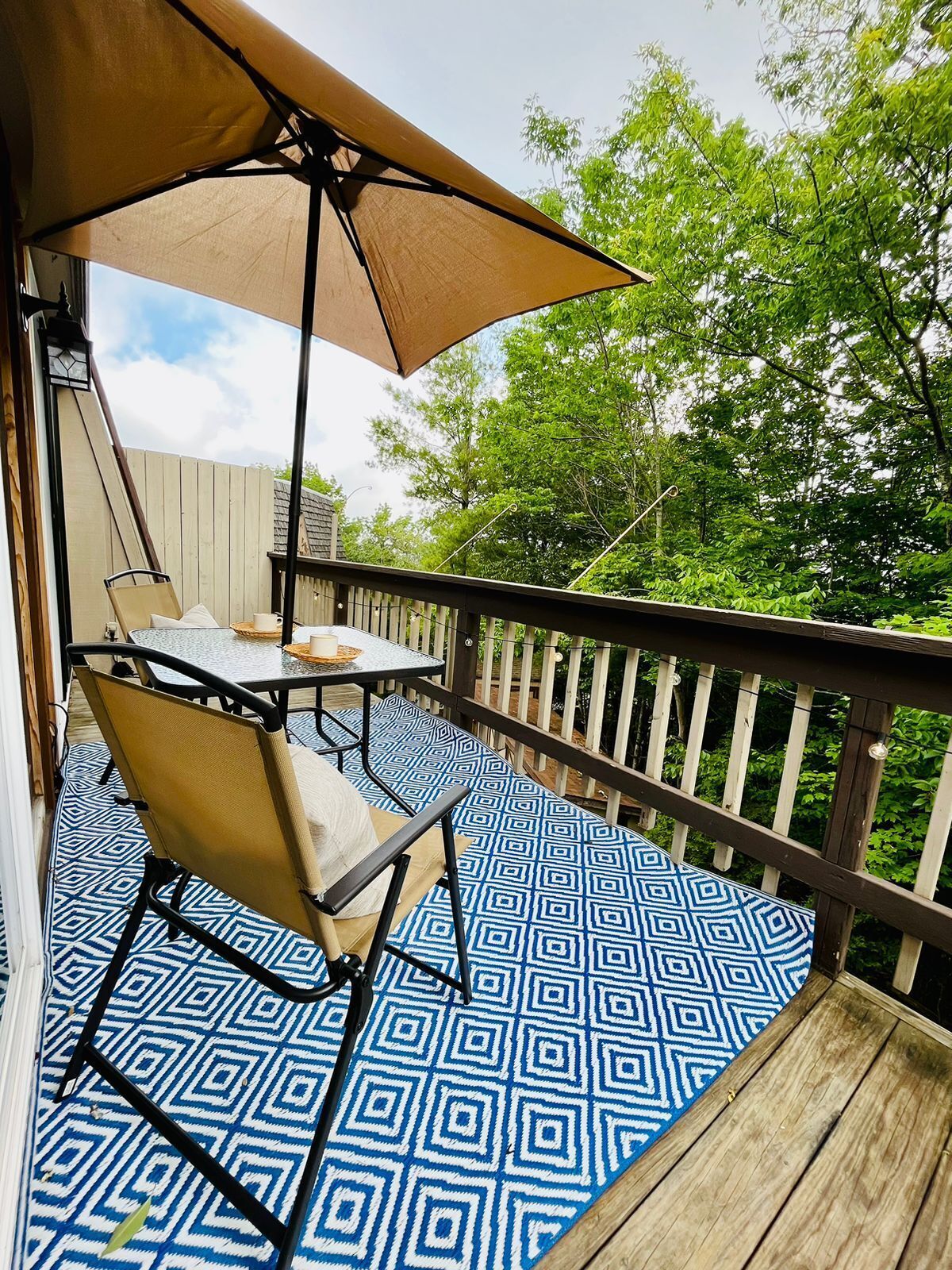 Un patio techado al aire libre con suelo estampado, una mesa y sillas, y una valla de madera.