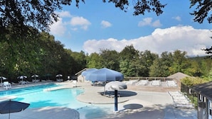 A swimming pool with a circular water feature, surrounded by lounge chairs and umbrellas. - Cozy Pet-Friendly Studio! Land of Oz ! Festivals! (Beech Mountain)