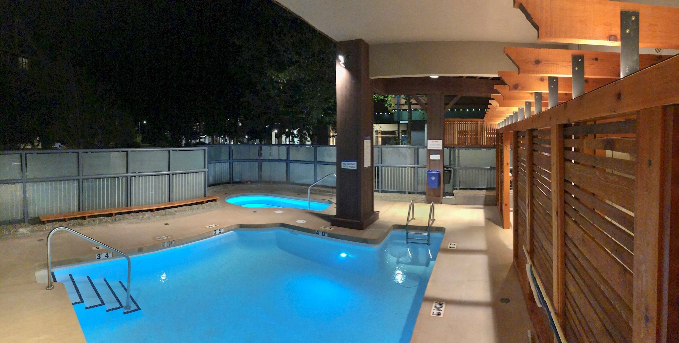 An indoor swimming pool with a wooden deck area and a covered seating section.