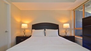 Una cama bien hecha con sábanas blancas, dos lámparas de noche con bases decorativas y un cabecero oscuro.