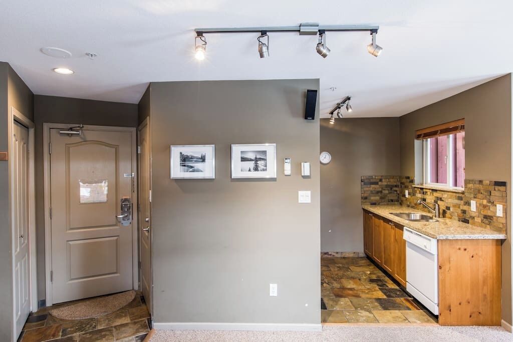 A modern kitchen with a stone backsplash, wooden cabinets, and a built-in dishwasher.