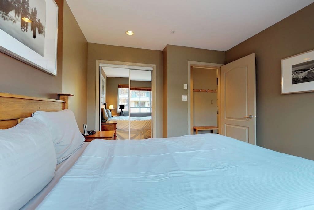 Une chambre d’hôtel avec un grand lit, une table de chevet, une lampe et une porte donnant sur une autre pièce.