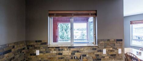 A kitchen with granite countertops, a double sink, a window with a view, and a stone backsplash.