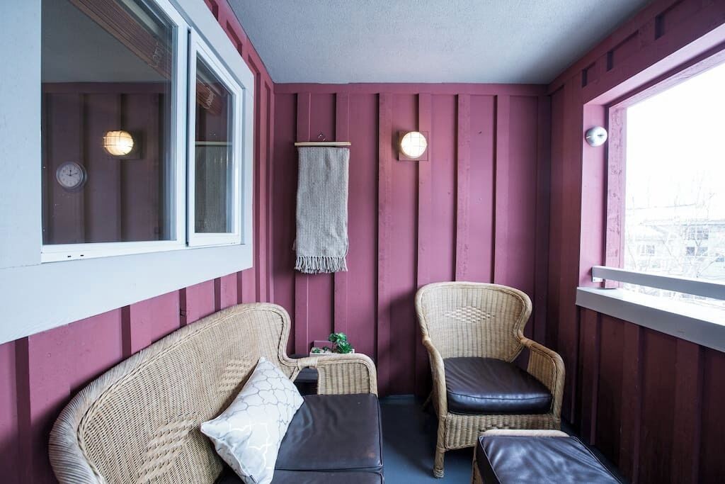 Quarto com duas cadeiras de vime, uma mesa pequena, um relógio e um candeeiro fixo na parede.