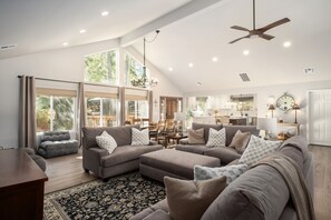 A spacious living room with a large sectional sofa, a dining area, and a kitchen in the background. - Brand New Rebuilt Remodeled Bass Lake house among the trees! Views of the lake! (Bass Lake)