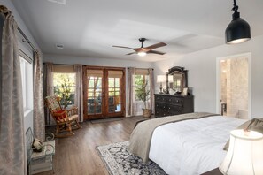 Een slaapkamer met een groot bed, een plafondventilator, een dressoir en een schommelstoel.