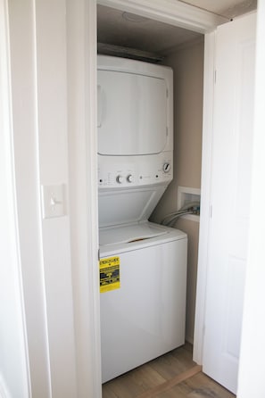 Un lavadero con lavadora y secadora apiladas, una etiqueta amarilla de eficiencia energética y suelo de madera.