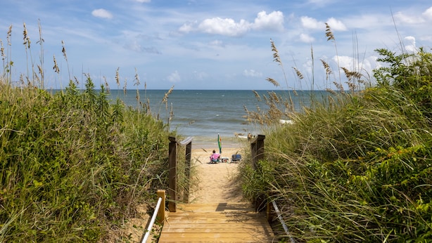 Une promenade en bois mène à une plage où une personne est assise sur une chaise de plage.