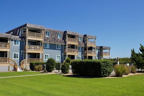 Un edificio residencial de varios pisos con balcones, un césped bien cuidado y un cielo azul despejado.