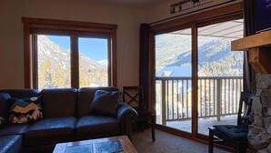 A cozy living room with a large window offering a mountain view, a stone fireplace, and a comfortable sofa.