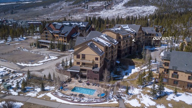A resort with multiple buildings, a swimming pool, and a ski slope in the background.