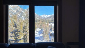 A room with a large window offering a view of a mountainous landscape with snow-covered peaks and a lake.