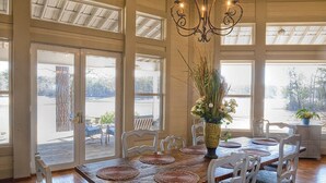Un coin repas avec une table en bois dressée pour quatre personnes, des chaises blanches et un lustre.