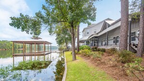 Une propriété au bord du lac, dotée d’un quai en bois, d’un espace salon couvert et d’une maison avec plusieurs balcons donnant sur l’eau.