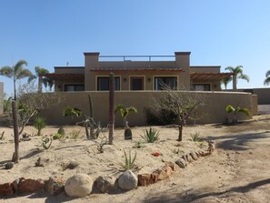 A modern house with a flat roof, surrounded by desert vegetation and rocks.