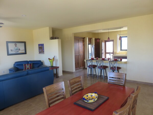 A living room with a blue sofa, a dining table with four chairs, and a kitchen area in the background.