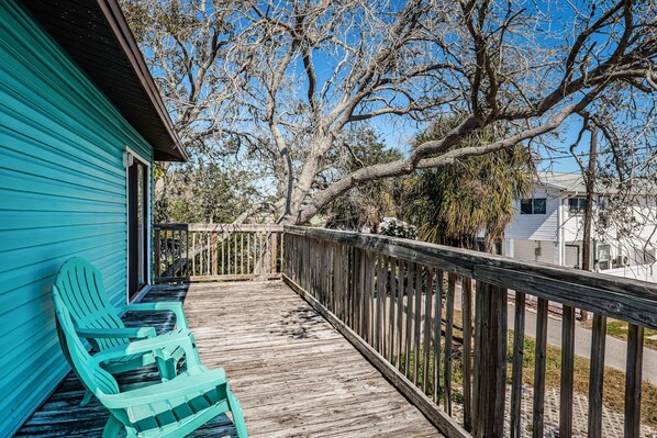 A wooden deck with a turquoise railing, a green Adirondack chair, and a view of a residential area with trees and houses.