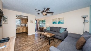 Ein modernes Wohnzimmer mit grauem Sofa, Couchtisch aus Holz und Deckenventilator.