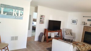 Una sala de estar con televisor sobre un mueble de madera, sofá, sillón y chimenea.
