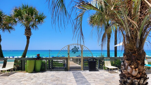 A paved walkway leading to a beach with palm trees and a sign indicating a guest shower area.