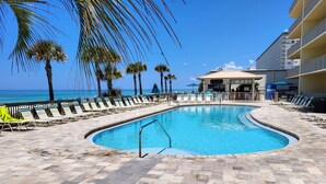 A pool area with lounge chairs and palm trees, a building with a sign, and a view of the ocean.