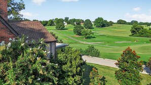 Een woonwijk met een bakstenen huis, een verzorgd gazon en een golfbaan op de achtergrond.