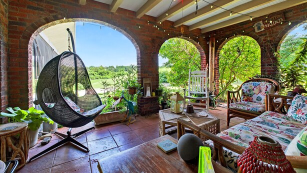 Une terrasse accueillante avec un fauteuil suspendu, des meubles en bois et un mur en briques.