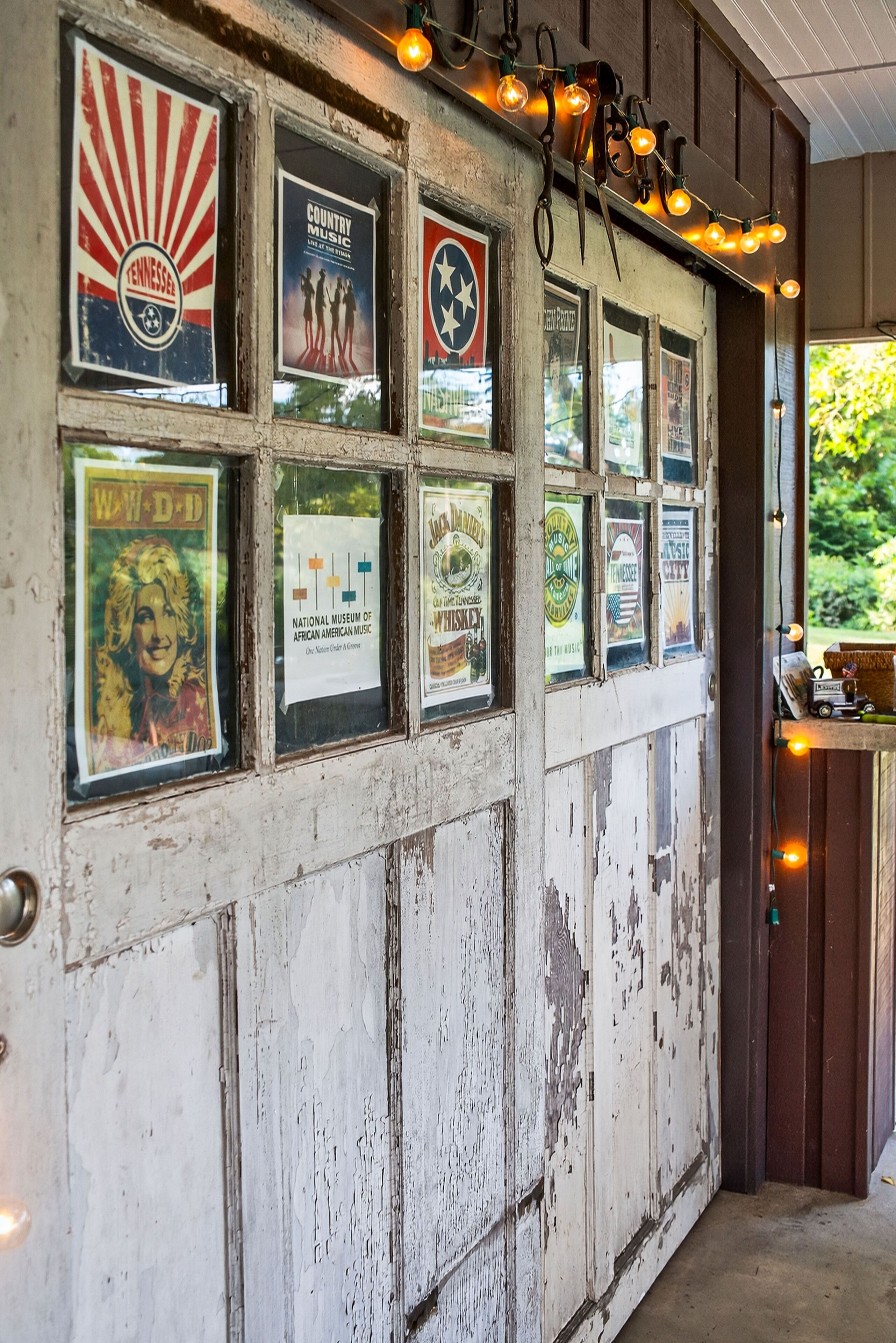 A wall with multiple framed posters, a rustic wooden door, and a string of lights.