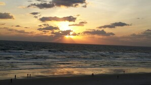 A beach with the sun setting over the ocean, people walking on the sand, and the sea in the foreground.