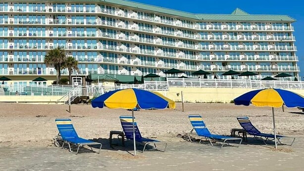A beachfront hotel with multiple balconies, beach umbrellas, and lounge chairs.