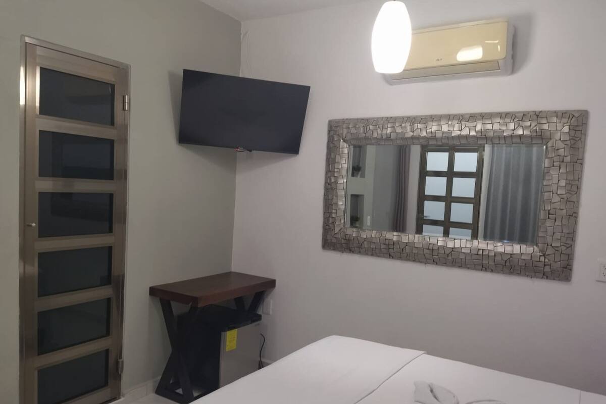 A hotel room with a bed, a desk, a television, and a mirror with a stone frame.