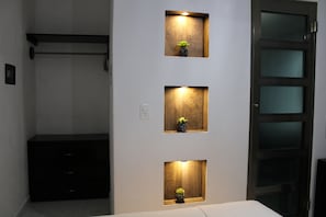 A room with a bed, a dresser, and three illuminated wall-mounted shelves with small potted plants.