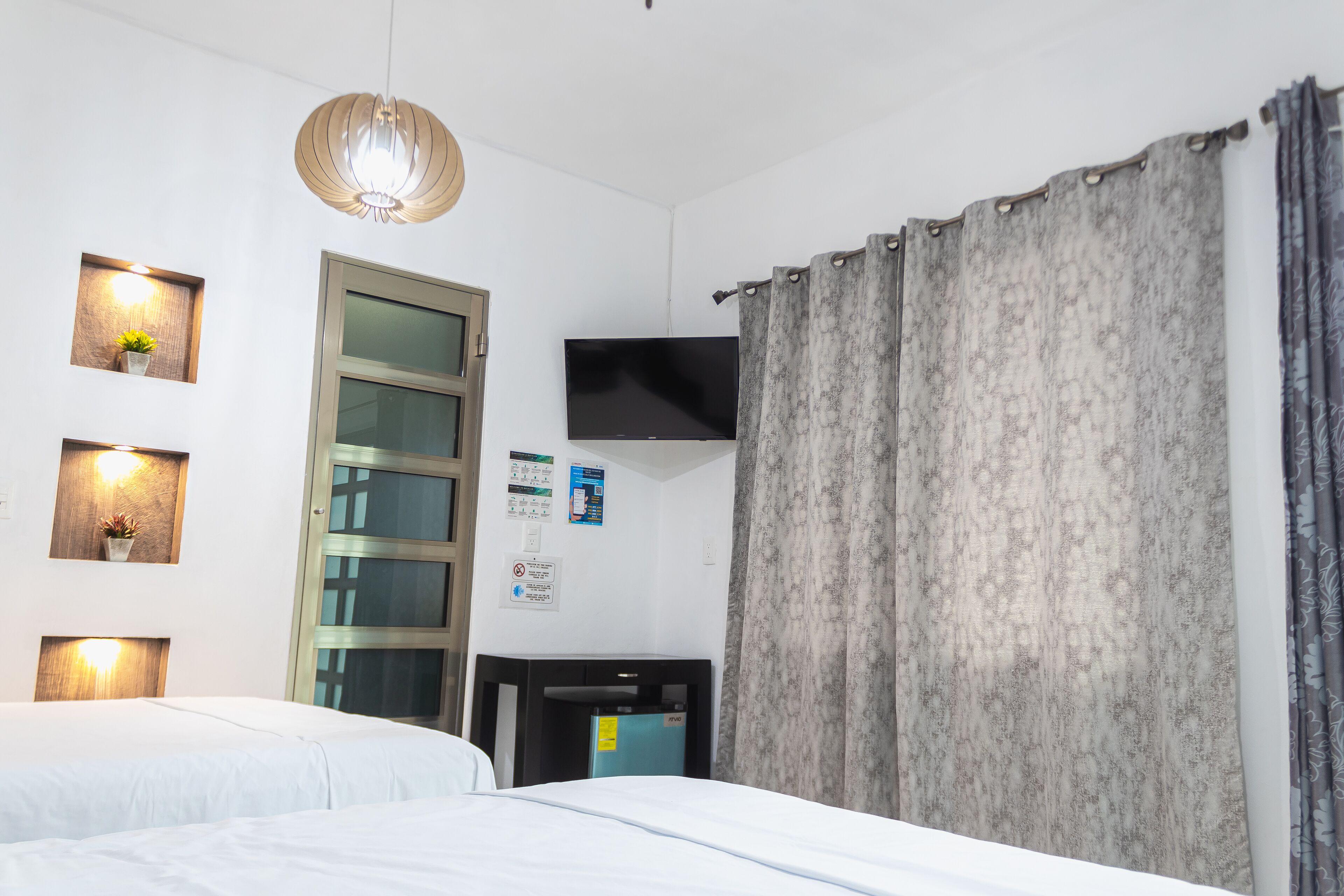 Una habitación de hotel con cama, televisión, escritorio y ventana con cortinas.