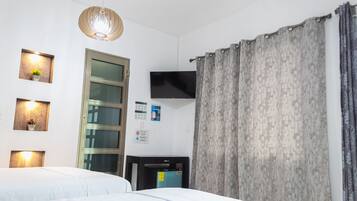 Una habitación de hotel con cama, televisión, escritorio y ventana con cortinas.