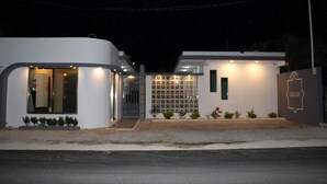 Um hotel moderno com fachada branca, entrada protegida por portão e um pequeno jardim.