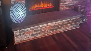 Une cheminée en briques surmontée d’un tableau encadré, un vase décoratif et un plancher en bois.