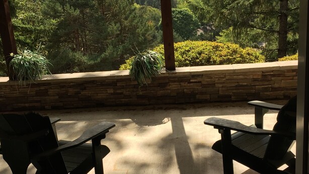 Un espace extérieur aménagé, abrité et doté de murs en pierre et de plantes en pot, offrant une vue sur un paysage boisé.