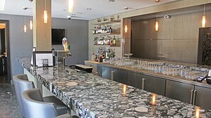 A bar area with a granite countertop, bar stools, and a variety of bottles and glasses. - Stunning Penthouse Suite (Canmore)