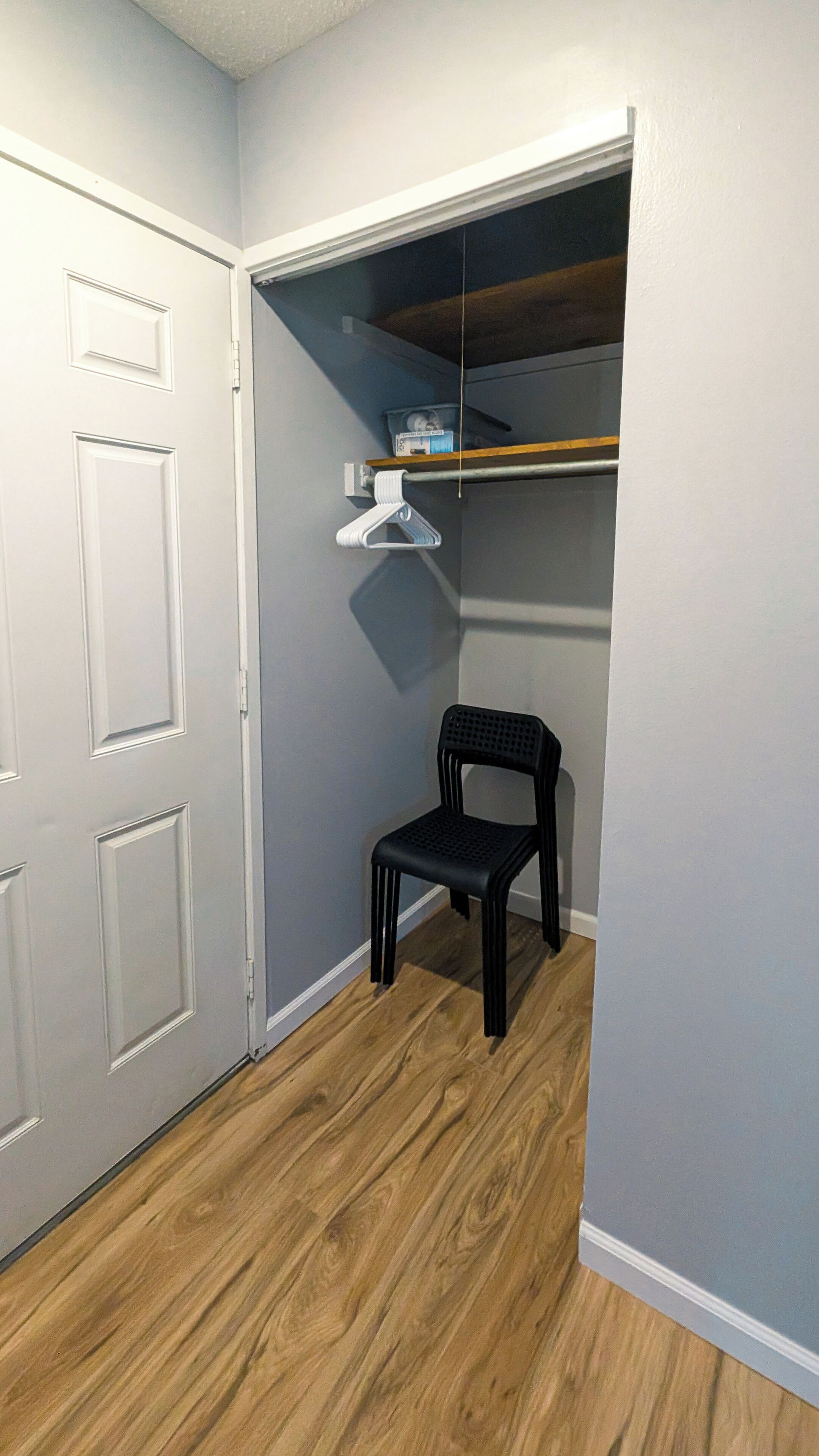 A closet with a wooden floor, a black chair, and a white hanging organizer.