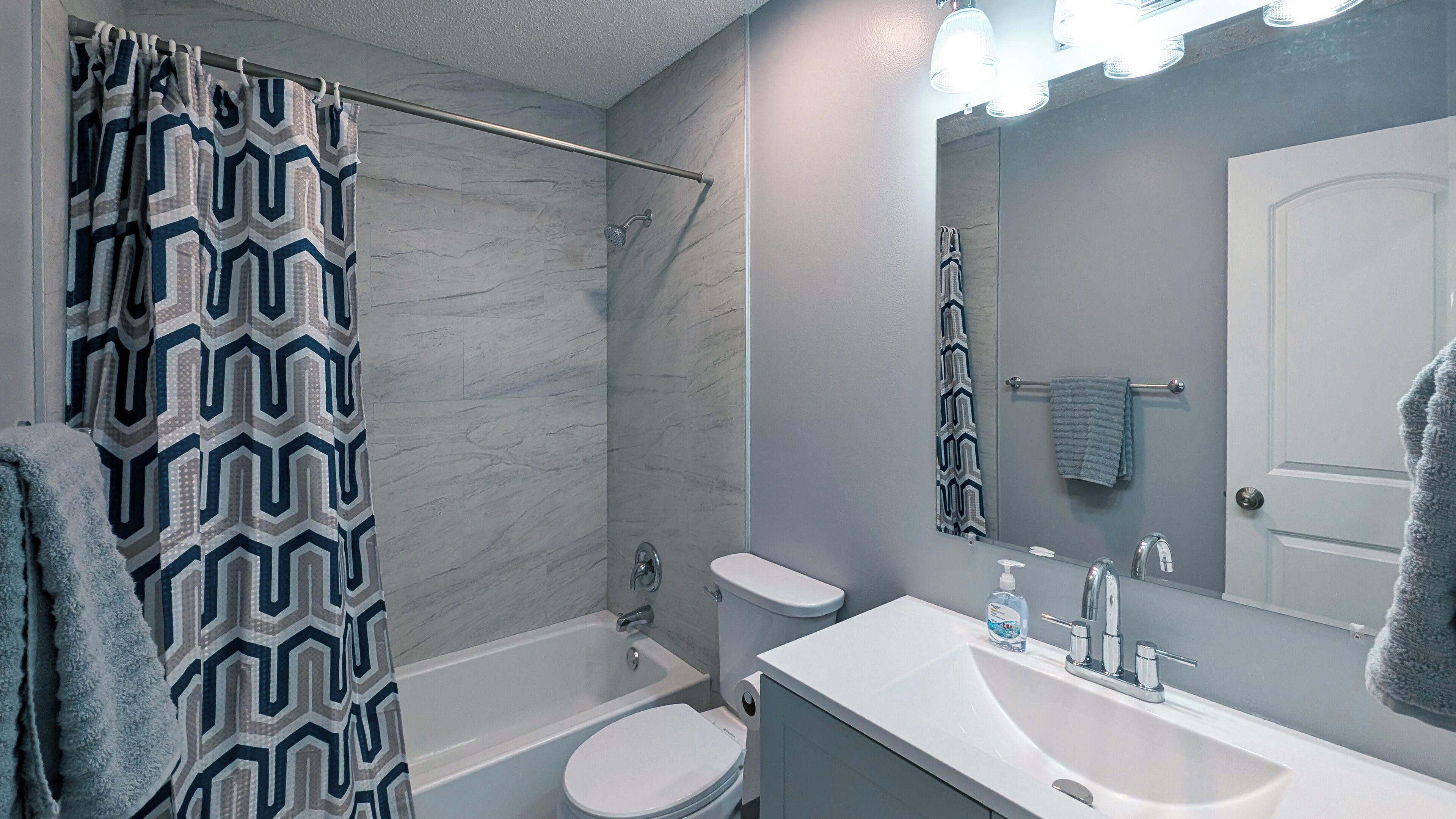 A bathroom with a shower, toilet, sink, and a mirror.