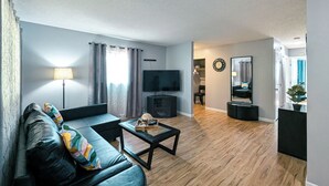 A modern living room with a leather sofa, a flat-screen TV, a coffee table, and a wooden floor. - Cute and affordable 3BDR duplex in Overland Park for up to 12 people! (Overland Park)