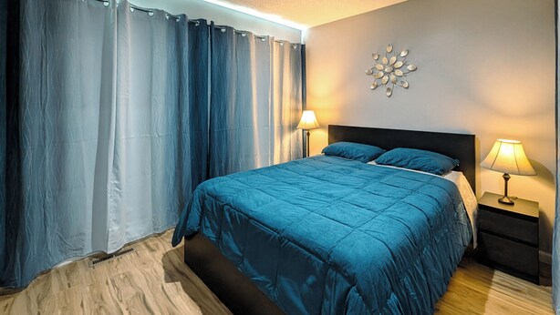 A bedroom with a bed, two bedside lamps, a wall clock, and a decorative wall piece. - Cute and affordable 3BDR duplex in Overland Park for up to 12 people! (Overland Park)
