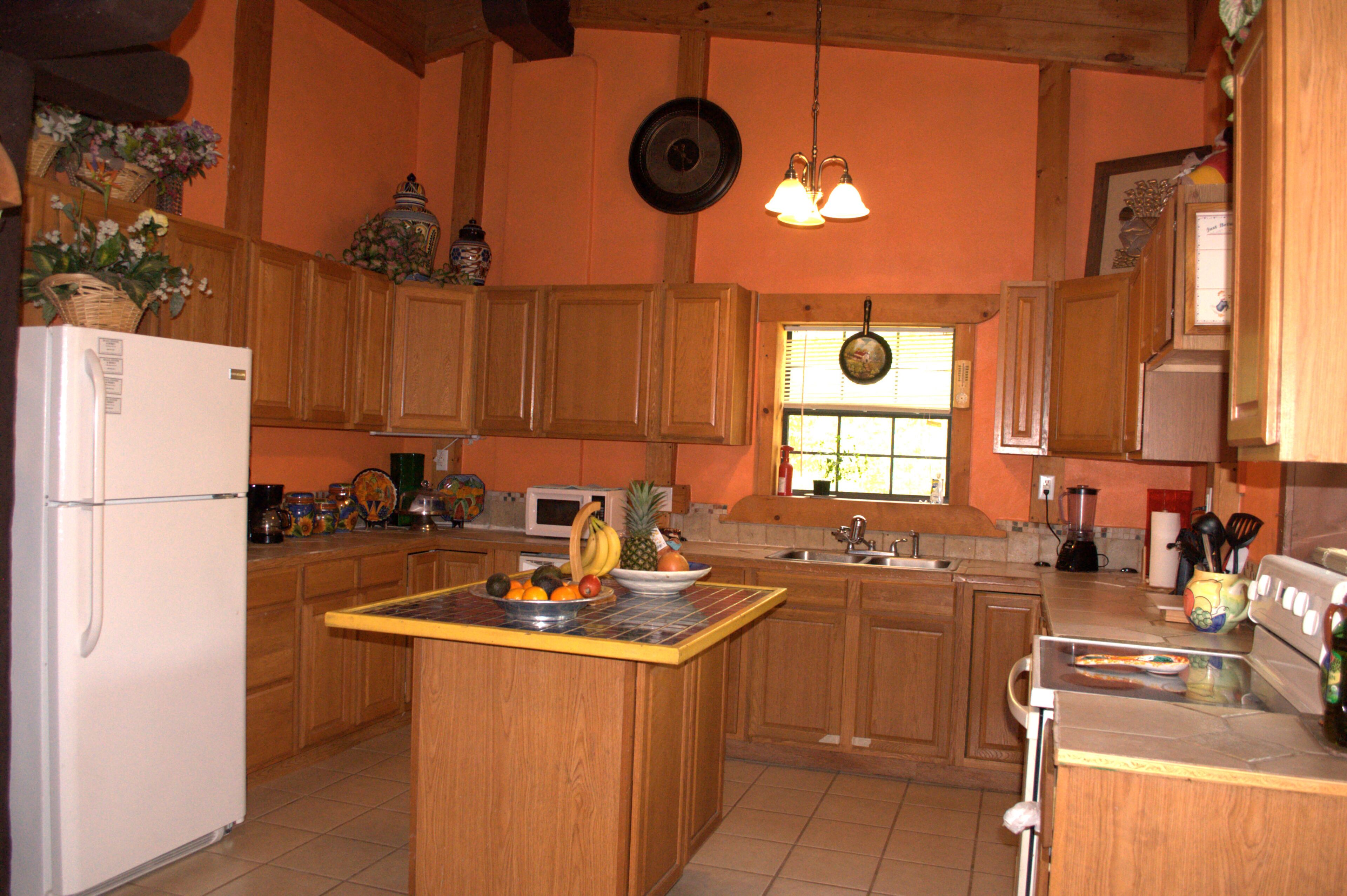 Una cocina con armarios de madera, una isla central con fruta, un refrigerador y una estufa.