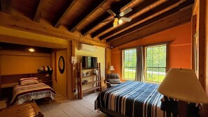 Un dormitorio acogedor con una cama grande, un escritorio y una silla. Hay un televisor en una estantería y una ventana con vistas a zonas verdes.
