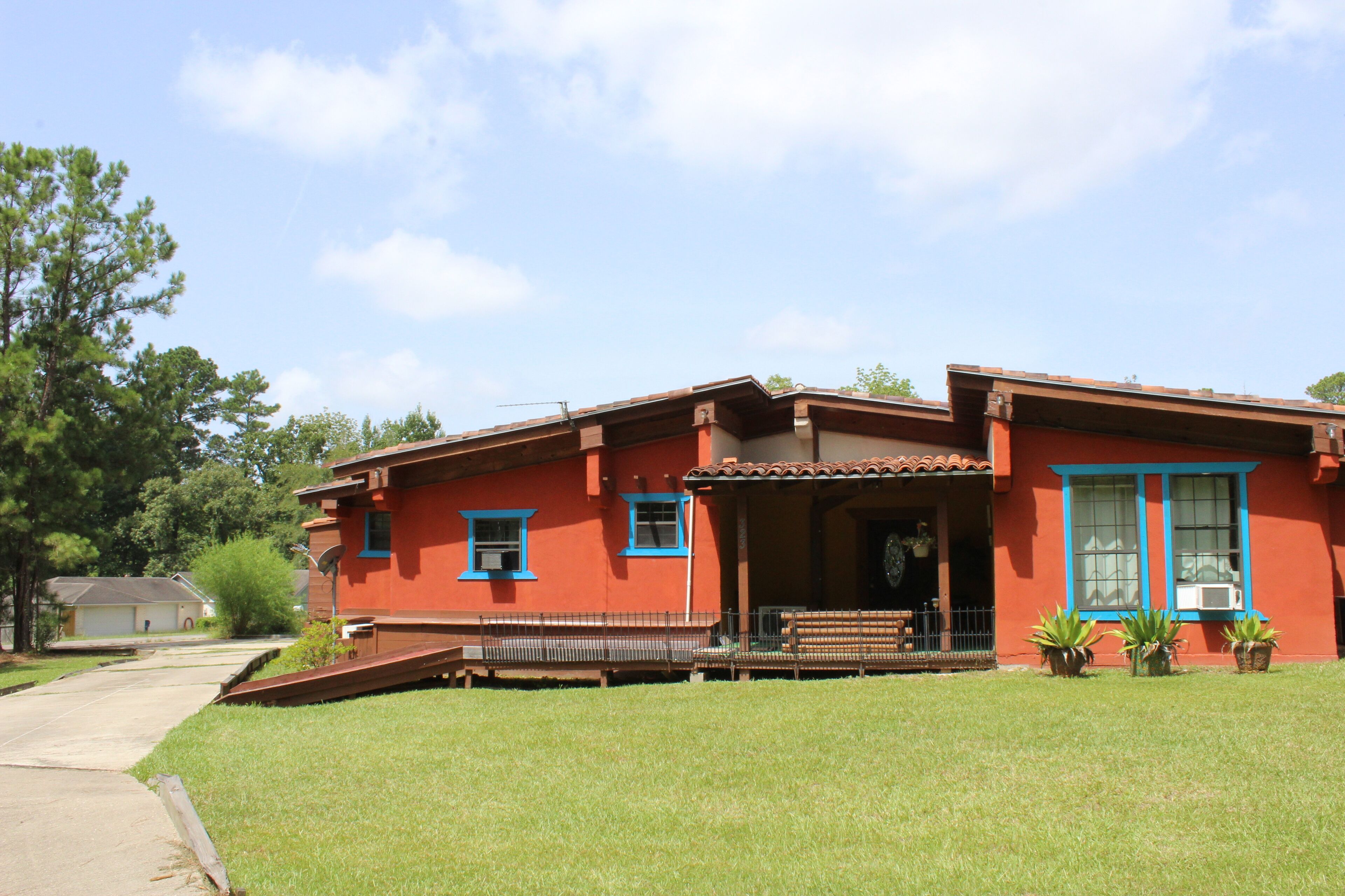 A red house with blue trim, a front porch, and a small front yard with potted plants.