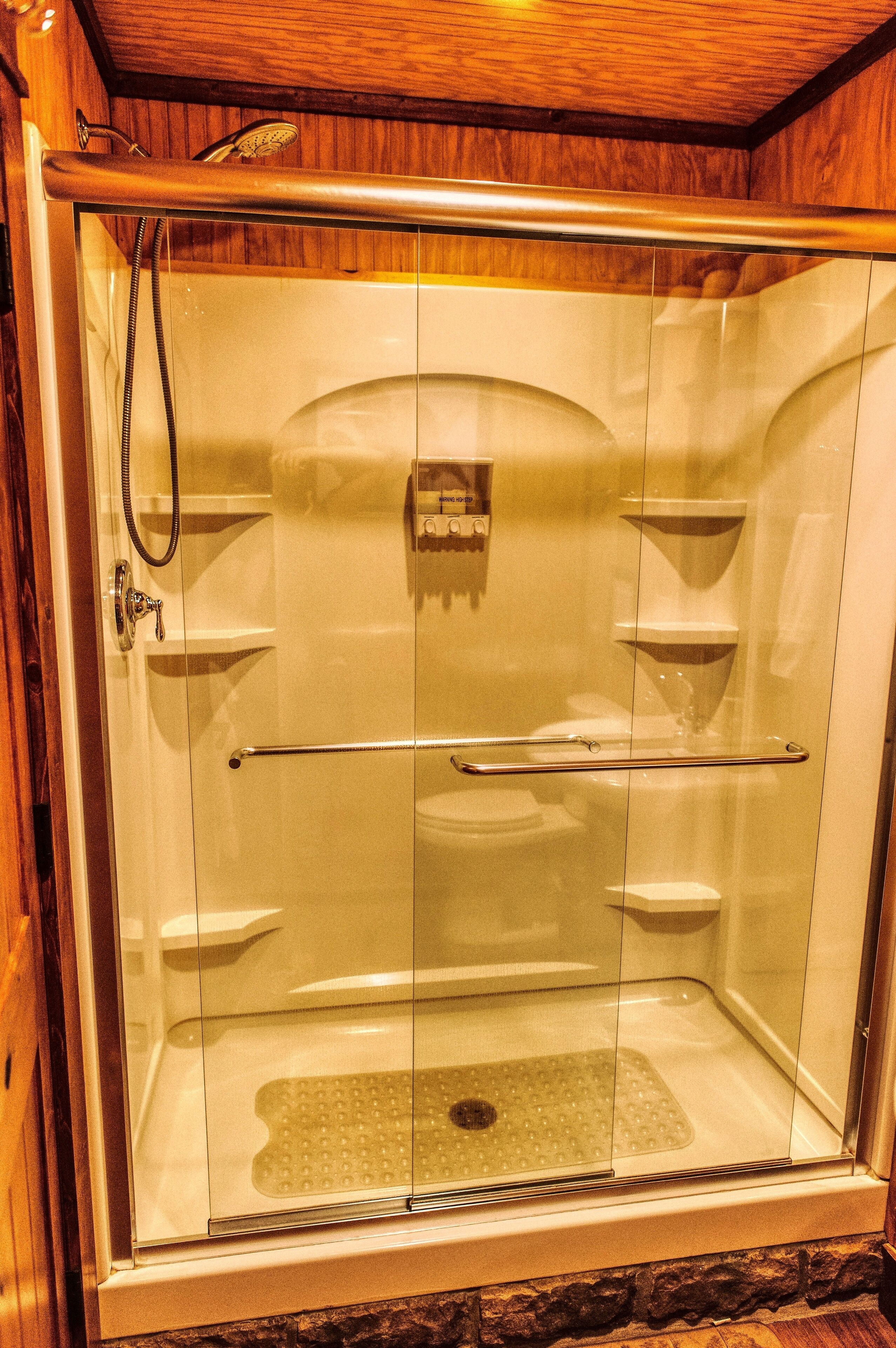 Een douchecabine met glazen wanden, een handdouche, een bediening voor de handdouche en een glazen deur.