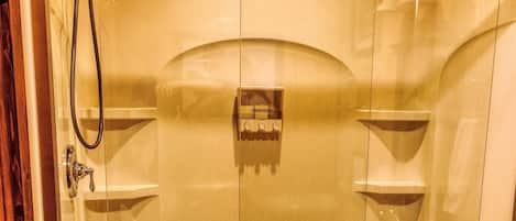 Een douchecabine met glazen wanden, een handdouche, een bediening voor de handdouche en een glazen deur.